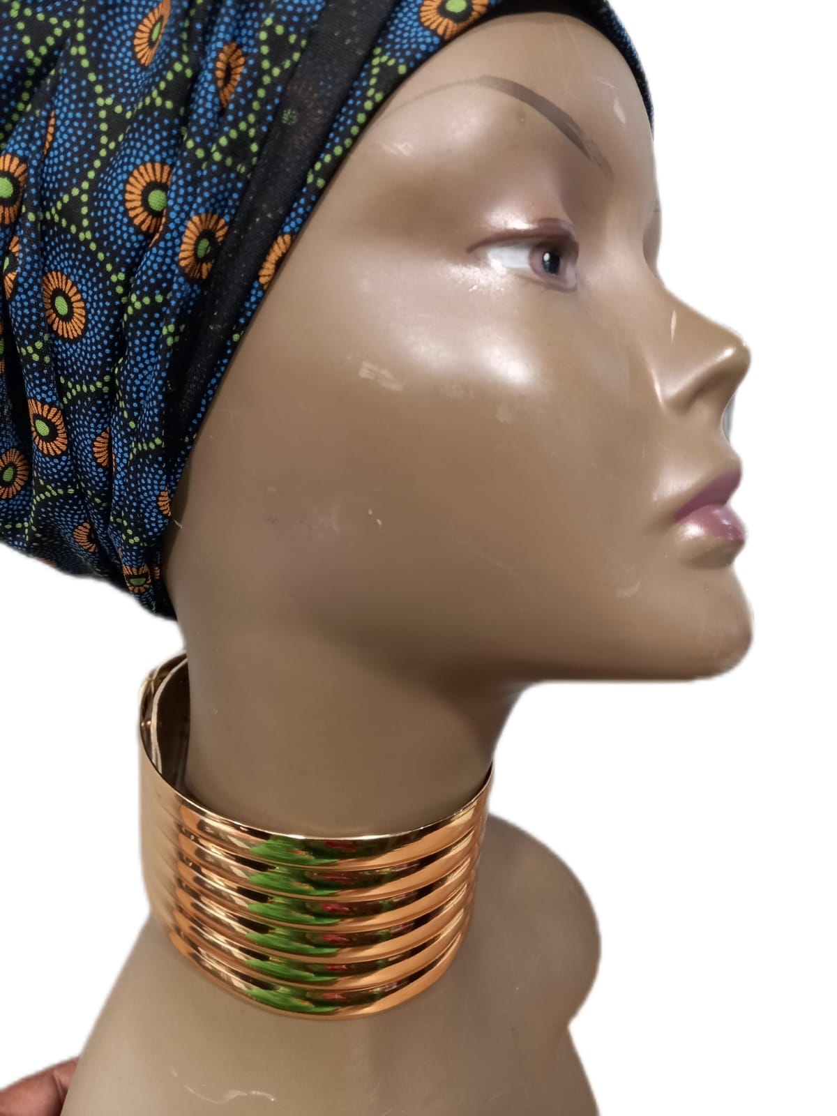 Mannequin head wearing a colorful headscarf and gold necklace on a white background